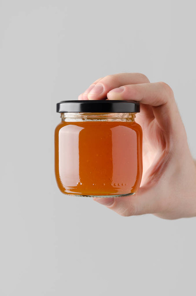 Apricot Jam Jar Mock-Up - Male hands holding a jam jar on a gray background - Fotoğraf, Görsel