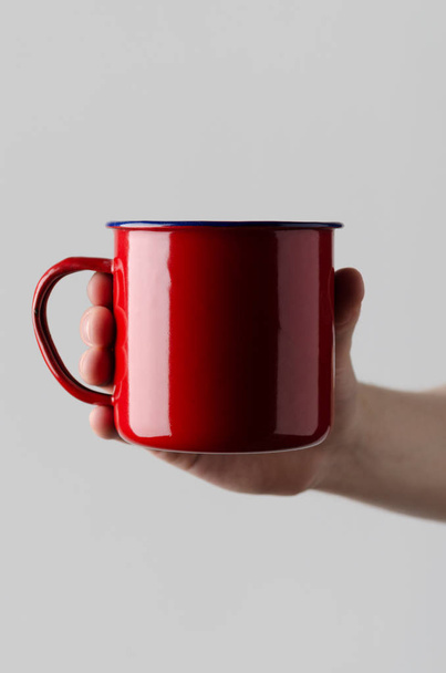 Red Enamel Mug Mock-Up - Чоловічі руки, що тримають емальований кухоль на сірому фоні
 - Фото, зображення