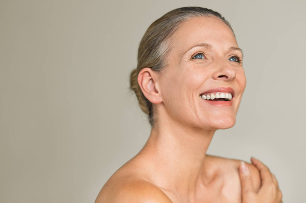 Portrait of a cheerful senior woman smiling while looking away isolated on gray background. Happy mature woman after spa massage and anti-aging treatment on face. - Foto, afbeelding