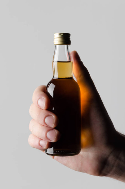 Espíritos em miniatura / Garrafa de Licor Mock-Up - Mãos masculinas segurando uma garrafa de licor em um fundo cinza
 - Foto, Imagem