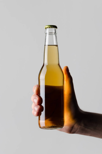 Beer Bottle Mock-Up - Male hands holding a beer bottle on a gray background - Foto, afbeelding