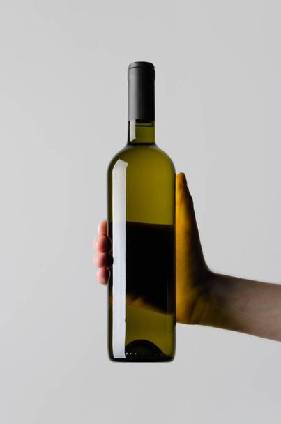 Κρασί μπουκάλι μακέτα-αρσενικό χέρια κρατώντας ένα μπουκάλι κρασί σε ένα γκρίζο φόντο - Φωτογραφία, εικόνα