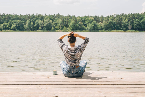 woman sitting on wooden dock looking at lake in sunny day - Photo, Image