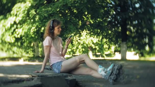 mujer patinando y escuchando música en los auriculares en el teléfono en el parque
 - Imágenes, Vídeo
