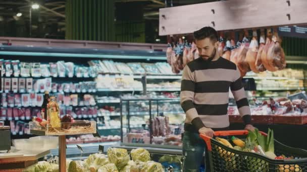 Komea nuori mies ostoksia tuoreita tuotteita supermarketissa laskemisesta kukkakaali hänen ostoskoriin copyspace elämäntapa elinvoimaa vegaani kasvissyöjä terveellistä ruokavaliota syöminen kuluttamista asiakas
 - Materiaali, video