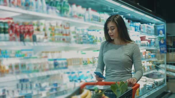 Vidám fiatal gyönyörű nő beszél a telefonon, mosolyogva, miközben vásárol a szupermarket copyspace bolt üzlet vásárlás vásárló fogyasztói ügyfél technológia kommunikációs hívás élelmiszer - Felvétel, videó