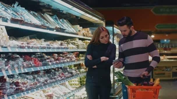 一緒にスーパーに買い物に男彼の妻 copyspace と食料をしながらスマート フォンのショッピング リストをチェック美しい幸せなカップル愛情熱愛情関係消費者 - 映像、動画
