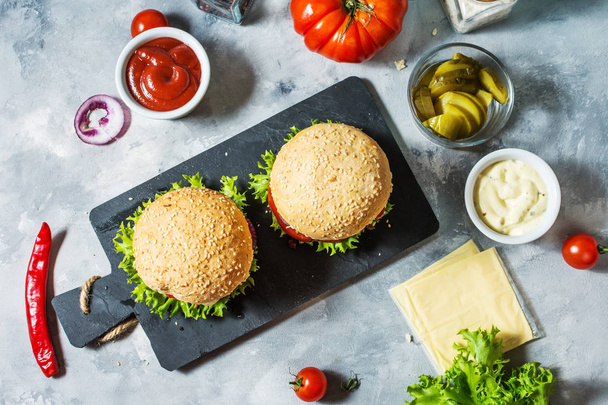 Вкусные домашние гамбургеры с говядиной, помидорами, сыром на бетонном фоне. Вид сверху
 - Фото, изображение