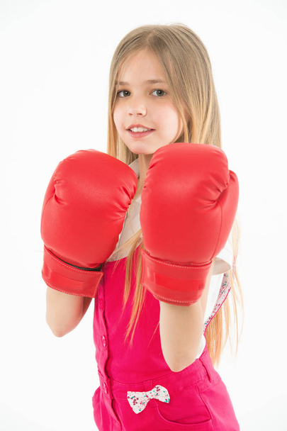 Little fighter before combat. Girl with long blond hair wearing huge red boxing gloves, sport concept. Kid in pink overalls isolated on white background. Brave girl ready to protect herself - Fotografie, Obrázek
