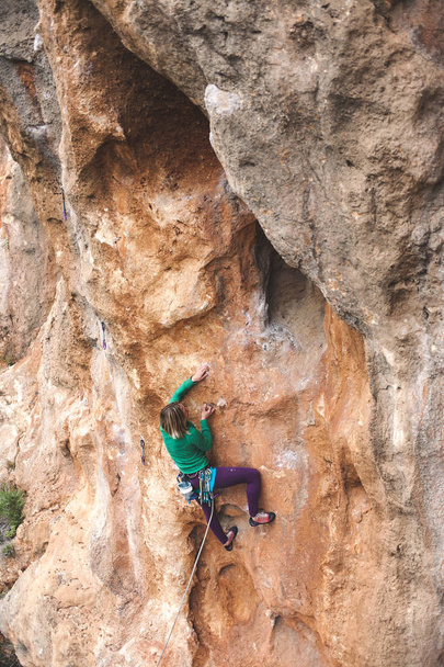 A woman climbs the rock. Climbing in nature. Fitness outdoors. Active lifestyle. Extreme sports. The athlete trains on a natural relief. - Photo, Image