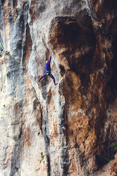 A rock climber on a rock. The girl is making an ascent. Sports in nature. Active lifestyle and fitness outdoors. An extreme hobby. Hardy woman. - Фото, изображение
