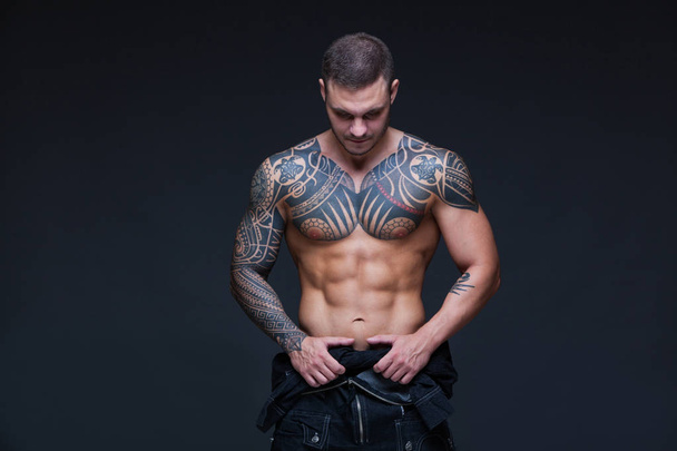 The man with a muscular naked torso with tattoos on the dark background. ABS - Foto, imagen