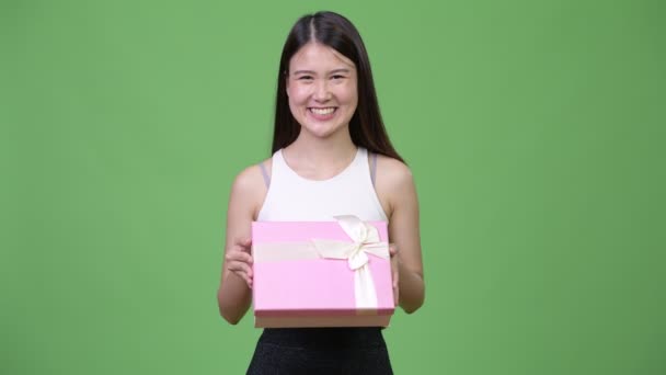 Young beautiful Asian businesswoman thinking while holding gift box - Filmati, video