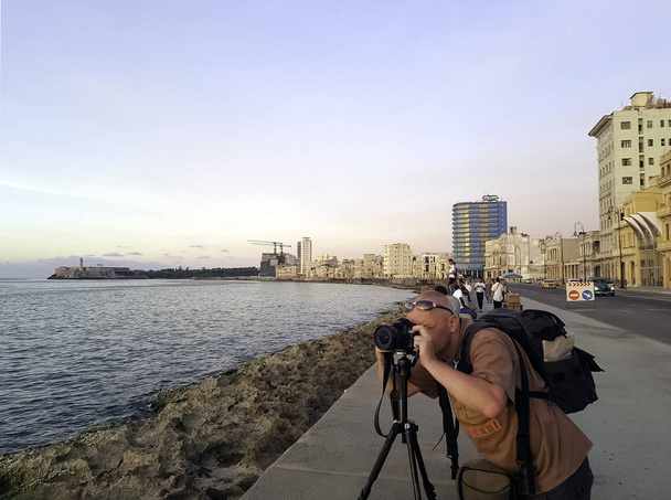 Photographer with camera during sunset with Atlantic Ocean, residential building and Morro Castle in background - Malecon, Havana, Cuba - Photo, Image