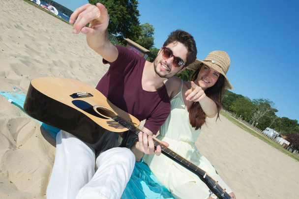 mladý muž se svou kytarou a přítelkyně na pláži - Fotografie, Obrázek