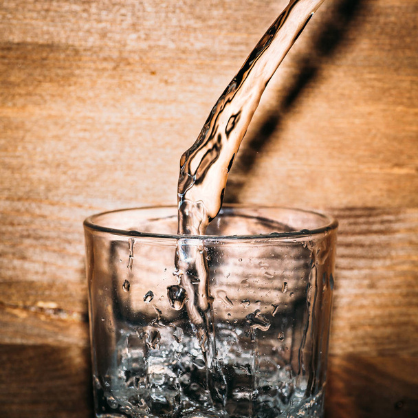 Pure fresh water is pouring into glass on wooden background close up, healthy drink - Фото, зображення