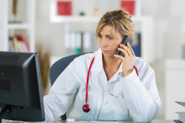female doctor sitting at her office while phoning her patient - Φωτογραφία, εικόνα