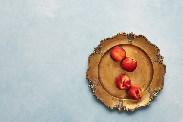 Flat lay of fresh nectarines fruits on rustic golden serving plate on light blue background. Top view with copy space. - Photo, image