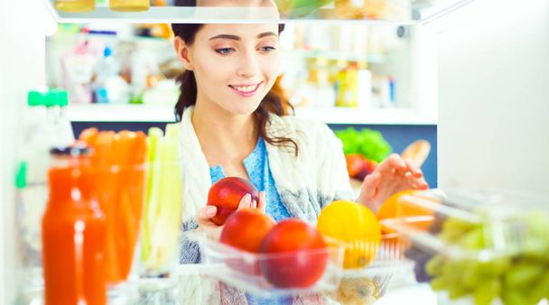 Porträt einer Frau, die neben einem offenen Kühlschrank voller gesunder Lebensmittel, Gemüse und Obst steht. Porträt einer Frau - Foto, Bild