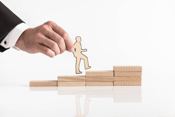Businessman holding a cutout of a man walking up steps formed by stacked wooden blocks in a concept of promotion and career success. - Photo, Image