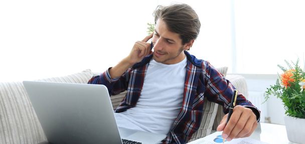young man discussing on a smartphone a financial graph at home. - Фото, изображение