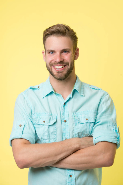 Cheerful consultant. Man smiling face posing confidently with folded arms yellow background. Man shop consultant looks cheerful confident and hospitable. Guy with bristle glad to help you in shop - Photo, Image