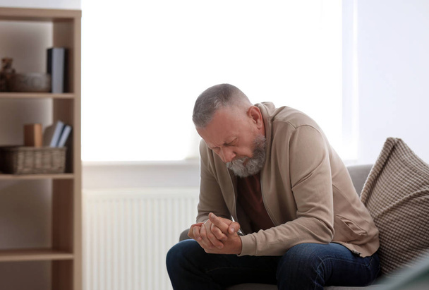 Depressed senior man sitting on sofa indoors - Foto, Imagen