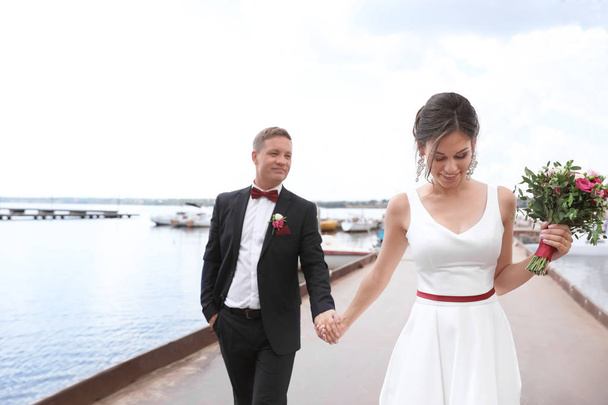 Happy newlyweds with beautiful bridal bouquet near river - Photo, Image