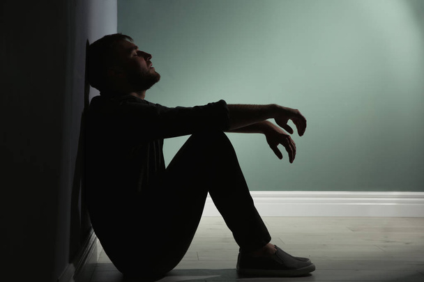 Depressed young man sitting on floor in darkness - Фото, изображение