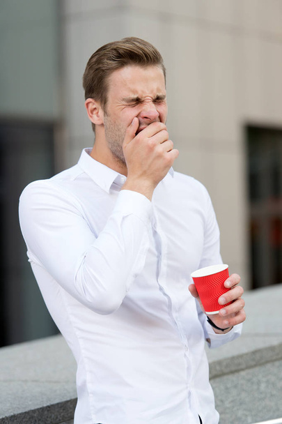 But first coffee. Man yawning drinks coffee urban background. Taking moment enjoy day. Businessman relaxing with coffee morning time. Guy handsome attractive guy yawning needs energy charge - Photo, image