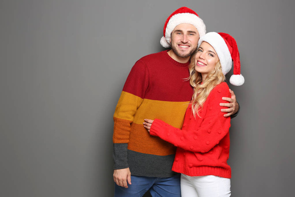 Young couple in Santa hats on grey background. Christmas celebration - Photo, image