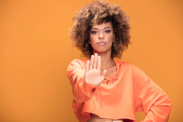Молодий афроамериканець жінка робить знак зупинки рукою, говорить ні, дивлячись на камеру. Жовтий студії фону - Фото, зображення