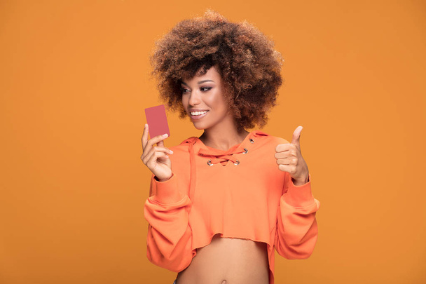 Young attractive african american woman holding credit card , standing on yellow background. - Фото, изображение