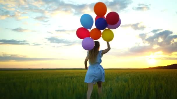 šťastná žena s balóny, které jsou spuštěny v poli pšenice při západu slunce - Záběry, video