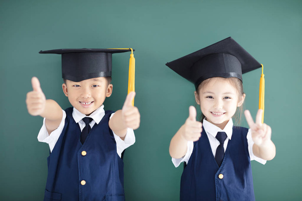Feliz chico y chica en la gorra de graduación mostrando los pulgares hacia arriba
 - Foto, imagen