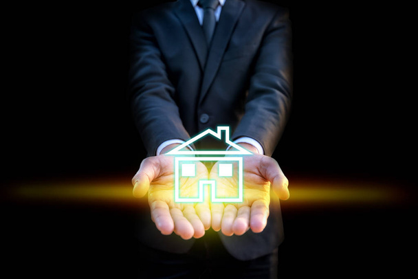 Concepto de bienes raíces, Manos de hombre de negocios inteligente ofrecen icono de la casa en la mano con efecto de luz de rayo sobre fondo negro
 - Foto, Imagen