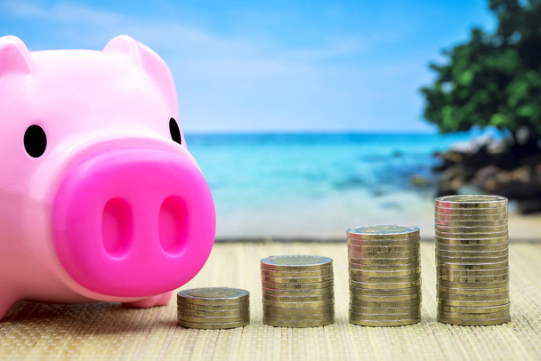 Budget vacation travel concept, piggy bank and stack coin on table with ocean background - Photo, Image