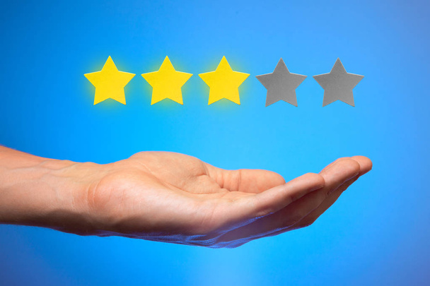 Three golden yellow stars out of five. Man holds star on the palm of his hand, puts rating, reviews - Photo, Image