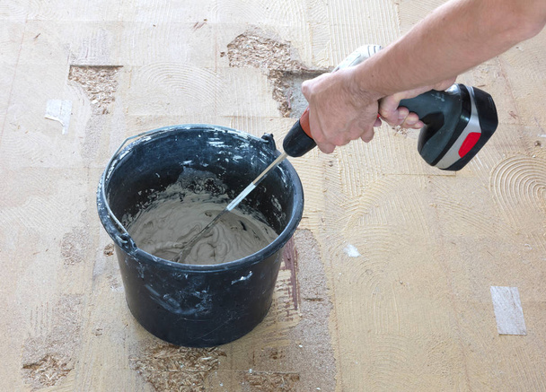 Man houdt boor mixer in zijn handen. Man is het mengen van grijs beton en eerste in de emmer. - Foto, afbeelding