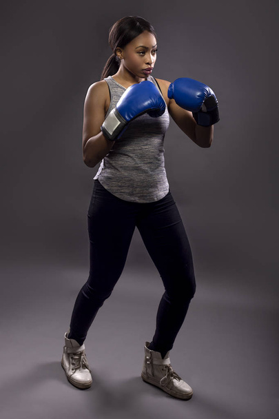 Black female wearing boxing gloves training or exercising.  She is posing with punches and depicts fitness or self-defense and martial arts. - Valokuva, kuva