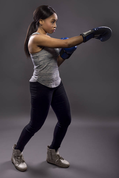 Black female wearing boxing gloves training or exercising.  She is posing with punches and depicts fitness or self-defense and martial arts. - Photo, Image