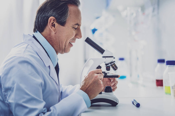 Bioengineer wearing white uniform looking into microscope - Фото, зображення