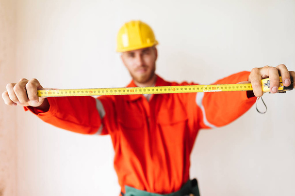 Primer plano capataz en ropa de trabajo naranja y amarillo hardhat celebración de cinta métrica sobre fondo blanco
 - Foto, imagen