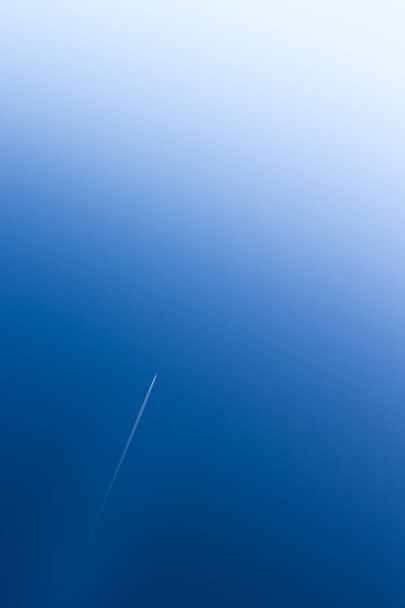 Vliegtuig vliegt op grote hoogte en verlaat zijn witte kielzog boven de blauwe lucht - Foto, afbeelding