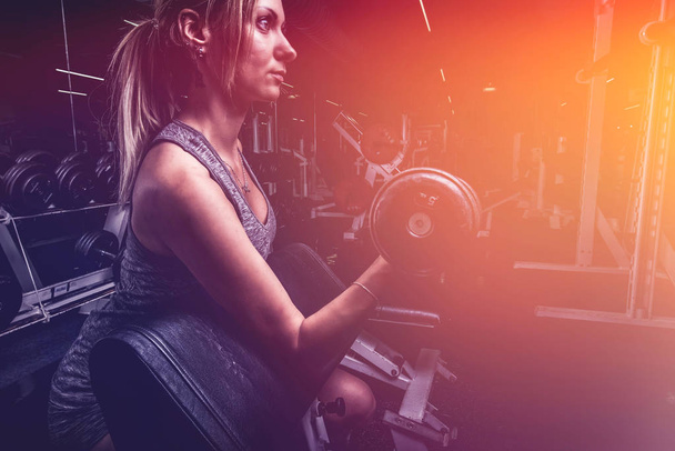Jeune belle femme faisant biceps curl avec EZ curl bar dans une salle de gym. Fille sportive faisant de l'exercice dans un centre de remise en forme
 - Photo, image