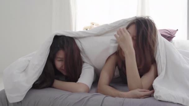 Beautiful young asian women LGBT lesbian happy couple hugging and smiling while lying together in bed under blanket at home. Funny women after wake up. LGBT lesbian couple together indoors concept. - Filmagem, Vídeo