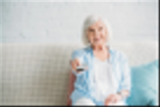 portrait of smiling senior woman with remote control watching tv on sofa at home - Foto, Imagen