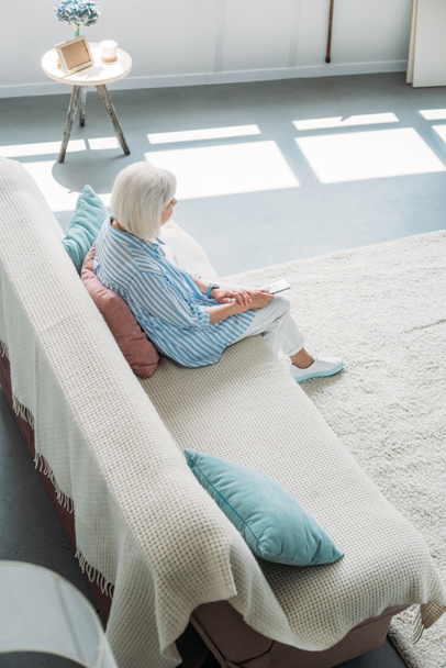 high angle view of senior woman with remote control watching tv on sofa at home - Fotografie, Obrázek