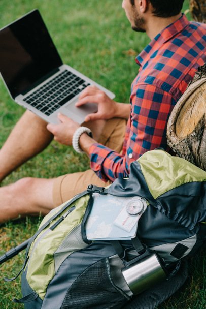 обрізаний знімок молодого чоловічого мандрівника, використовуючи ноутбук на траві
 - Фото, зображення
