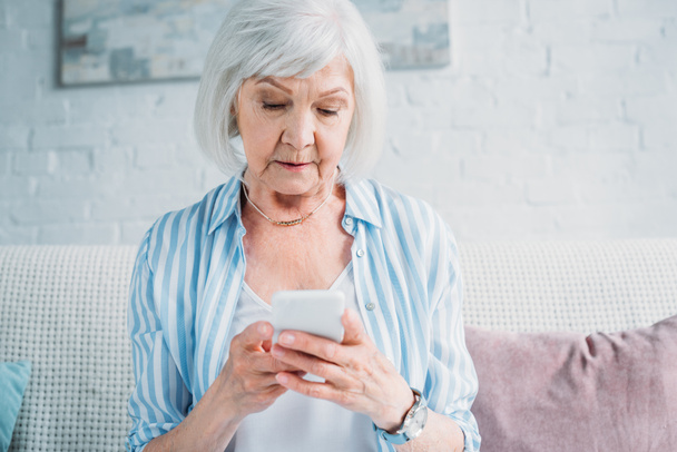 портрет пожилой женщины с помощью смартфона во время отдыха на диване дома
 - Фото, изображение